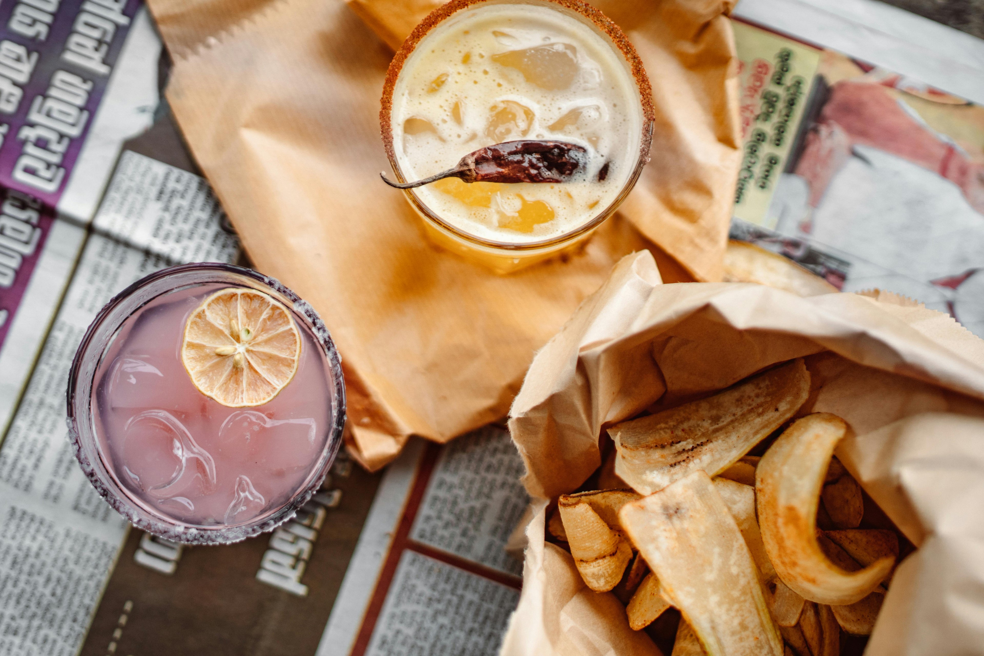 A flatlay image of cold iced teas with snacks laid out on a paper