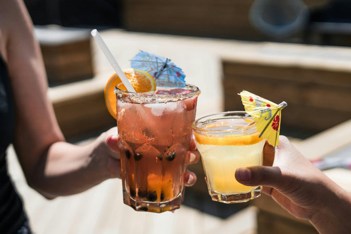 An image of two people holding two mocktail glasses in hand