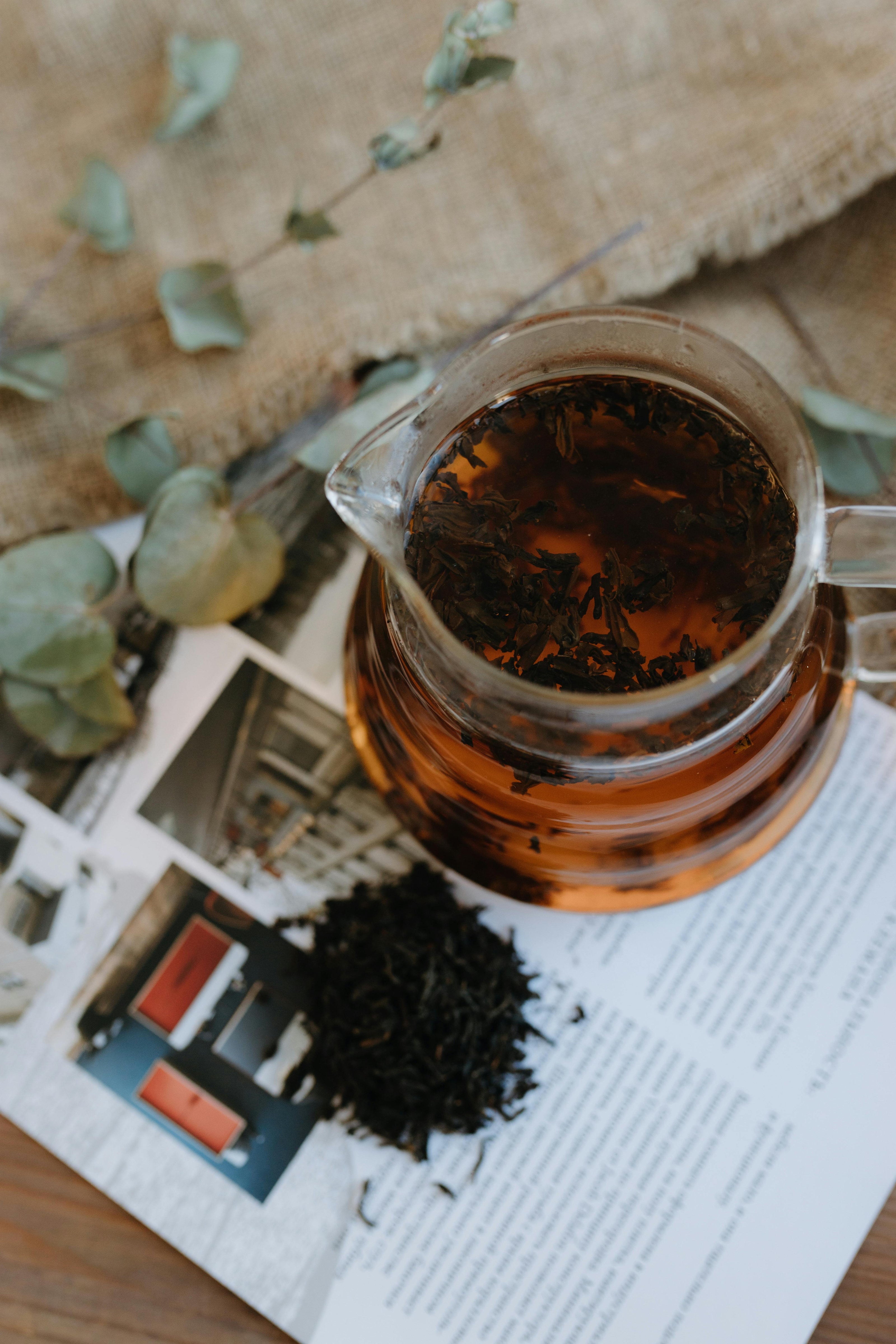 Glass jug filled with freshly brewed Ceylon black tea, placed on an open magazine with loose tea leaves nearby